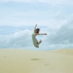 woman in white dress jumping on brown sand during daytime